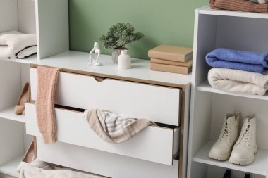 Klozetli raflar ve dağınık giysiler dağınık oturma odasında yeşil duvarın yanında, yakın çekim.