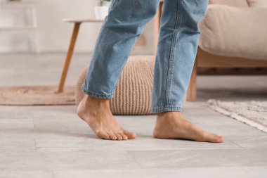 Çıplak ayaklı, kot pantolonlu, evde ısıtmalı kadın bacakları.
