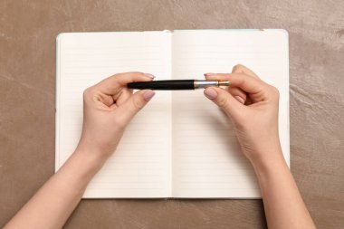 Kahverengi zemin üzerinde defter ve kalem olan eller