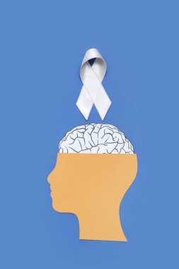 Beyni ve mavi arka planda gri farkındalık kurdelesi olan kağıt insan kafası. Kanser kavramı