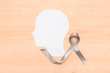 Ak ahşap zemin üzerinde gri farkındalık kurdelesi olan kağıt insan kafası. Beyin kanseri kavramı