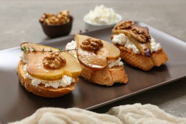 Gri arka planda ricotta peynirli ve cevizli armut bruschetta tabağı.