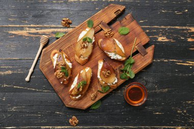 Siyah ahşap zemin üzerinde ricotta peynirli, cevizli ve naneli armut bruschetta.