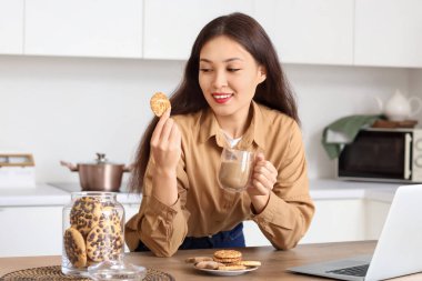 Mutfakta bir fincan kakao ve kurabiyeli genç Asyalı kadın