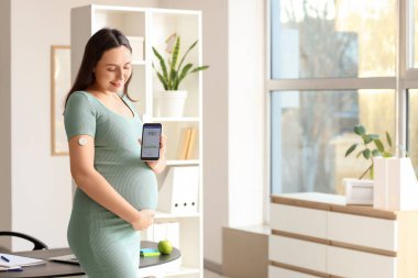 Ofisinde glikoz sensörü ve cep telefonu olan hamile bir iş kadını. Gebelik Diyabet Konsepti