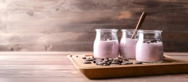 Lezzetli yoğurt kavanozları ve ahşap arka planda çikolata parçaları.