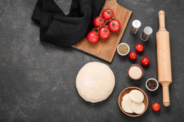 Siyah arka planda pizza hazırlamak için ham hamur ve malzemeler
