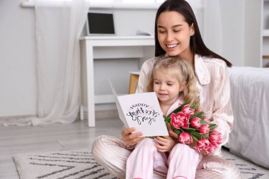 Küçük kız, mutlu annesini bir buket güzel çiçek ve tebrik kartıyla kutluyor. Anneler Günü kutlaması
