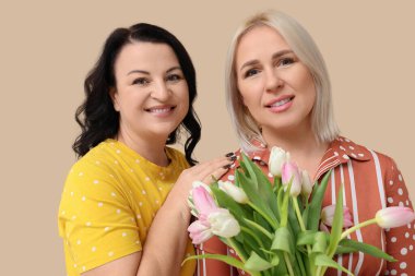 Bej arka planda güzel lalelerle dolu buketi olan mutlu olgun kadınlar. Uluslararası Kadınlar Günü