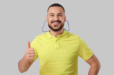 Kulak tıkacı olan genç adam gri arka planda baş parmak gösteriyor.