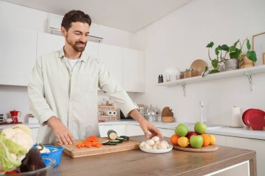 Mutfakta taze sebze pişiren yakışıklı sakallı adam.