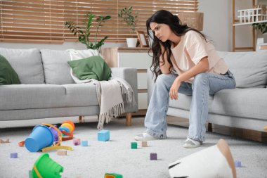 Evde dağınık çocuk oyuncakları arasında dinlenen yorgun genç bir anne. Stres kavramı