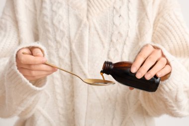 Kadın beyaz arka planda şişeden kaşığa öksürük şurubu döküyor.