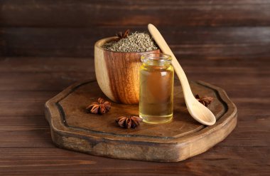 Bir şişe yağlı kaşık, anason yıldızları ve ahşap zemin üzerinde kurumuş tohumlar.