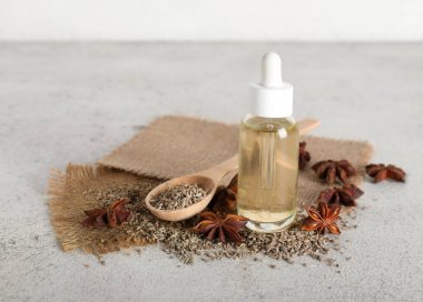 Anason yıldızlı bir şişe yağ, tahta kaşık ve gri grunge masasında kurutulmuş tohumlar.