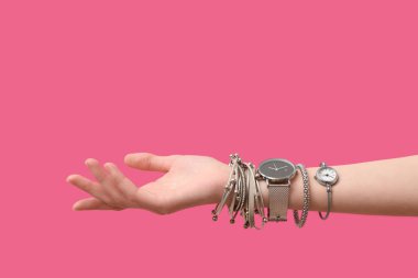 Kol saatleri ve pembe arka planda gümüş bilezikleri olan bir kadın.