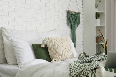 Yatak odasındaki beyaz tuğla duvarın yanında yumuşak yastıklı yatak