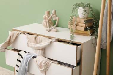 Oturma odasında yeşil duvarın yanında dağınık giysilerle tuvalet, yakın plan.