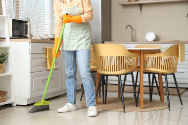 Genç kadın mutfakta yerleri süpürüyor.