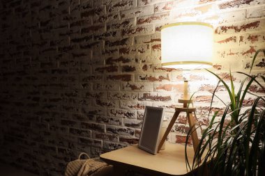 Karanlık odada tuğla duvarın yanında çerçevesi olan parlak bir lamba.