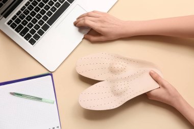 Ortopedik tabanlı ve bej arka planda dizüstü bilgisayarı olan bir kadın.