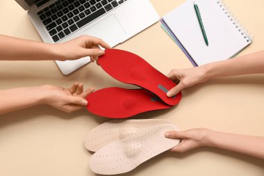 Ortopedik tabanlı kadın eller ve bej arka planda dizüstü bilgisayar.