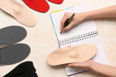 Ortopedik tabanlı bir kadın arka planda deftere yazı yazıyor.