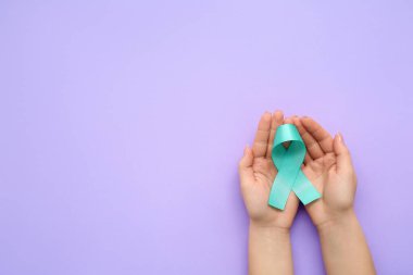 Leylak arka planında turkuaz kurdeleli kadın eller. Rahim Sağlığı Bilinci Ayı