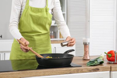 Genç bir kadın mutfakta kızarmış sebzelere tuz ekliyor.