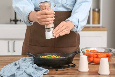 Genç bir kadın mutfakta kızarmış sebzelere tuz ekliyor.