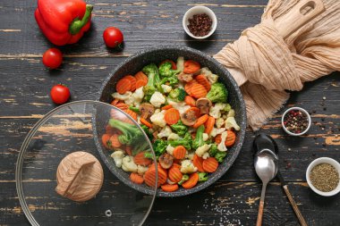 Kızartma tavası ve siyah ahşap arka planda lezzetli sebzeler.