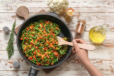 Kızarmış sebzeleri kızartılmış tavada karıştıran genç bir kadın.