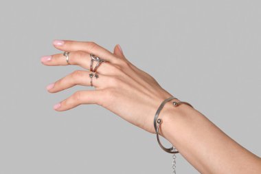 Beyaz arka planda gümüş yüzükler ve bileziklerle kadın eli, yakın plan.