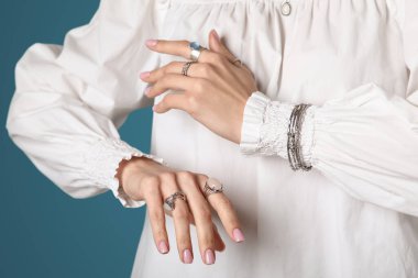 Siyah turkuaz arka planda gümüş yüzükler ve bileziklerle şık beyaz bluzlu güzel bir bayan.