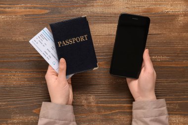 Modern cep telefonlu kadın eller, pasaport ve bilet ahşap arka planda, yakın plan