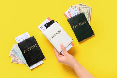 Sarı arka planda kadın eli ve pasaportlar, biletler ve kredi kartı.