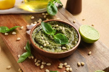 Bir kase lezzetli pesto sosu, fesleğen yaprağı ve bej arka planda çam fıstığı.
