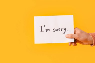 Elinde kağıt olan genç adam. Turuncu arka planda özür dilerim.