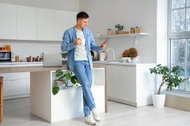 Mutfakta çay fincanı ve cep telefonu olan yakışıklı bir genç.