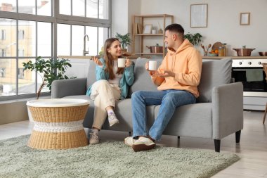 Yakışıklı genç adam ve kız arkadaşı evdeki kanepede çay içiyorlar.