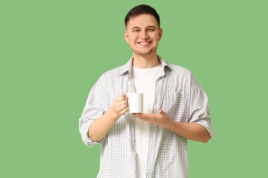 Yeşil arka planda çay fincanı olan yakışıklı genç adam.