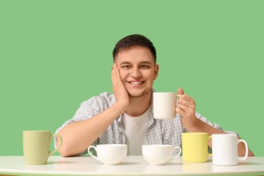 Farklı kupaları olan yakışıklı genç adam yeşil arka plana yaslanıyor.