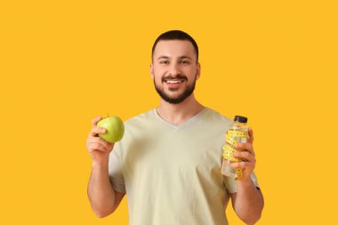 Taze elmalı genç bir adam, bir şişe su ve sarı arka planda şerit. Sağlıklı gıda konsepti