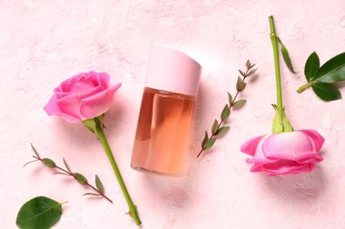 Bir şişe parfüm ve açık pembe arka planda güzel güller.