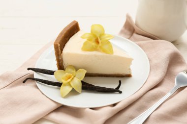 Vanilyalı tatlı peynirli kek dilimi ve beyaz ahşap arka planda çubuklar.