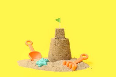 Güzel kumdan kale, sarı arka planda plaj oyuncakları.
