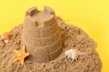 Sarı arka planda deniz yıldızları ve deniz kabukları olan güzel bir kumdan kale. Yakın plan.