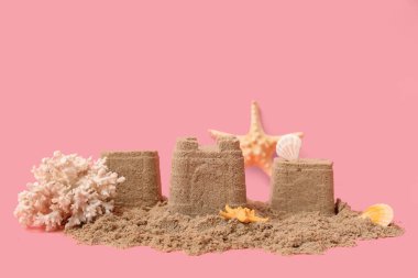 Pembe arka planda deniz kabukları, deniz yıldızları ve mercanlarla güzel bir kumdan kale.