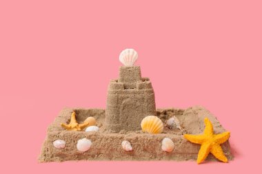 Pembe arka planda deniz yıldızları ve deniz kabukları olan güzel bir kumdan kale