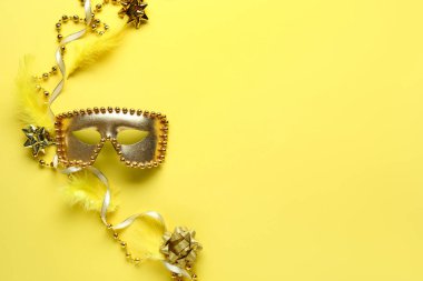 Sarı arka planda tüyleri ve boncukları olan güzel altın karnaval maskesi